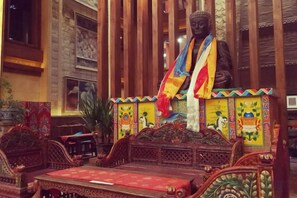 A room with a large Buddha statue, ornate wooden furniture, and traditional decor.