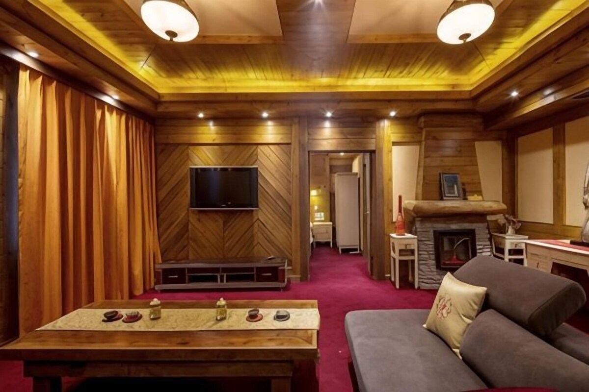 Un salon chaleureux avec un plafond en bois, un téléviseur à écran plat fixé au mur, une cheminée et un canapé.