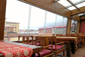 A restaurant with wooden tables and chairs, large windows, and a view of buildings. - Da Zang Sunlight Hotel (Zoige)