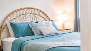 A bed with a woven headboard, teal and white bedding, and a bedside lamp.