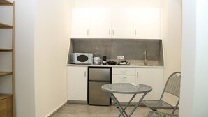 Een compacte keuken met witte kastjes, een magnetron, een waterkoker en een kleine koelkast. Er is een opklapbare tafel en twee stoelen.