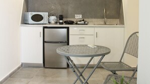 Een kleine keuken met witte kastjes, een magnetron, een kleine koelkast en een ronde tafel met twee stoelen.