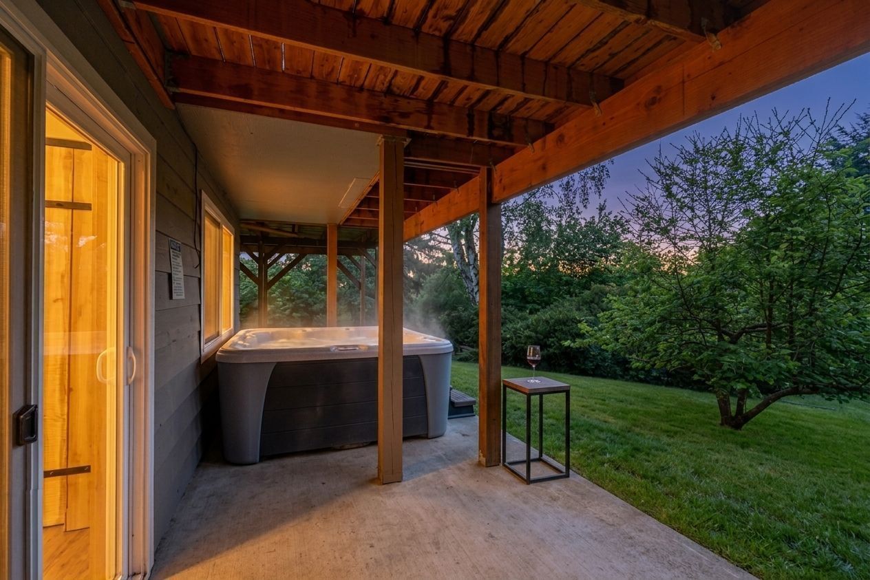 Un bain à remous installé sous une pergola en bois, avec vue sur un jardin et des arbres.