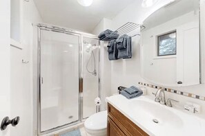 Une salle de bain moderne avec une douche à parois de verre, un lavabo blanc avec un meuble-vasque en bois et un porte-serviettes avec des serviettes pliées.