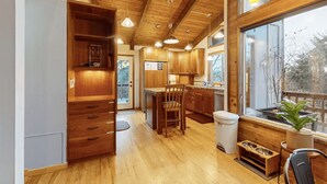 A spacious kitchen with wooden cabinets, a central island, and a large window providing a view of the outdoors. - Cozy Home•Hot Tub•Sauna•EV Charger•Bay & Dining 5m (Bay City)
