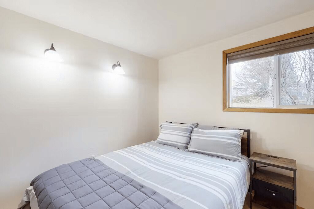 Ein Schlafzimmer mit einem Bett, zwei Wandleuchten, einem Fenster und einem Nachttisch.