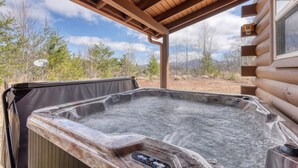 Un jacuzzi bajo una pérgola de madera con vistas a árboles y montañas.