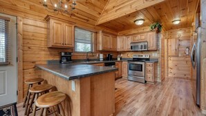 Cocina tipo cabaña de madera con una isla central, taburetes de bar, estufa, microondas y refrigerador.