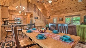 Interior de una cabaña de madera con comedor, cocina y escalera.
