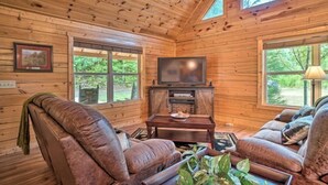 Un interior de cabaña acogedor con paredes de madera, un sofá de cuero, un televisor y una chimenea.