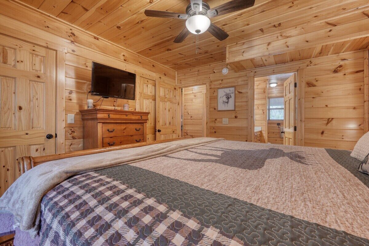 A wooden cabin bedroom with a bed, dresser, and ceiling fan.
