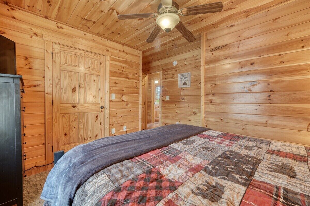 Une chambre dans une cabane en bois, avec un lit, un ventilateur de plafond et une porte.