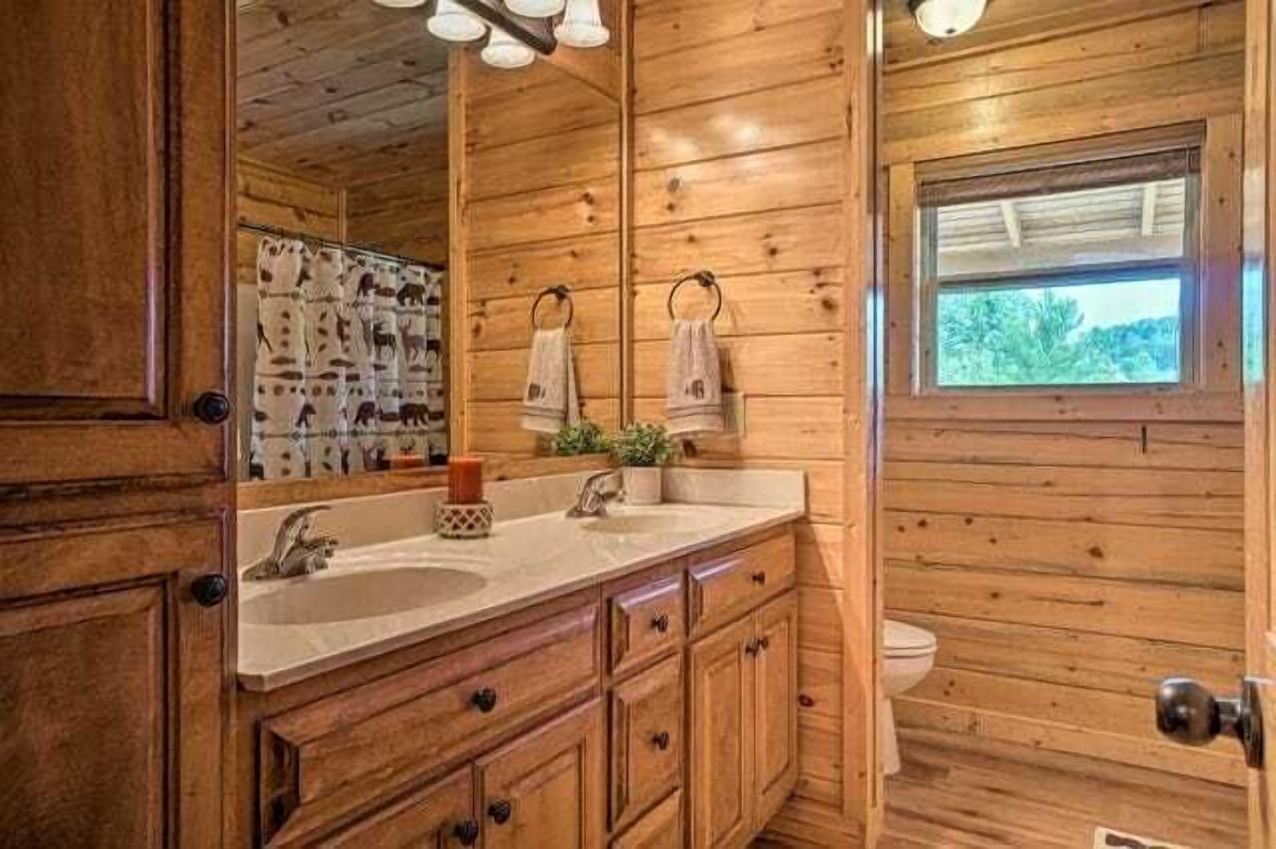 Une salle de bain rustique, avec des murs en bois, un grand miroir, deux lavabos et une fenêtre.