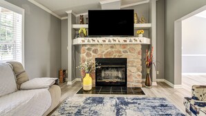 A living room with a stone fireplace, a flat-screen TV mounted above it, a sofa, and a blue patterned rug. - 8 Mi to Jordan Lake: Spacious New Hill Home (New Hill)