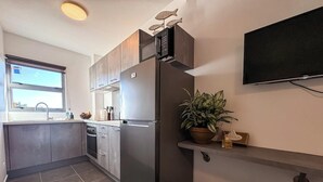 Cocina moderna con refrigerador de acero inoxidable, horno empotrado y microondas. Cuenta con una ventana que proporciona luz natural, una planta en maceta y un taburete de bar.