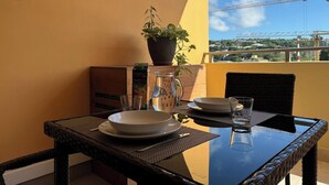 Una mesa de comedor con platos, una jofaina y un vaso en un balcón con vistas a una grúa de construcción y edificios.