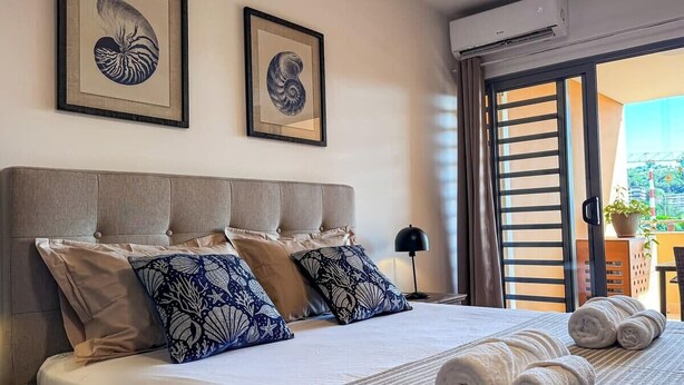 Una cama bien hecha con una colcha a rayas, dos almohadas con estampado floral y dos cuadros en la pared.