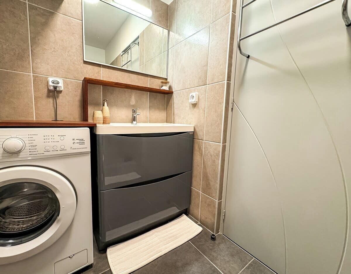 A compact bathroom with a washing machine, a sink, and a shower.