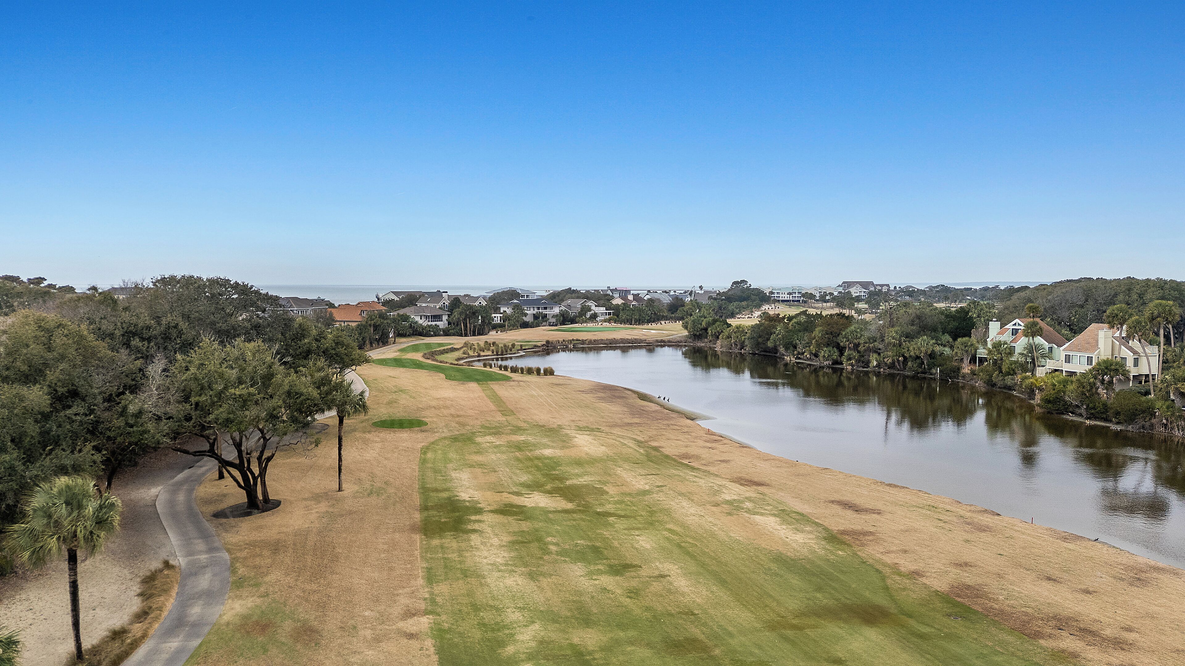 A golf course with a water body, surrounded by residential houses and trees.