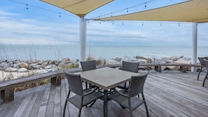 A covered outdoor seating area with a table and chairs, overlooking a rocky shoreline. - Seabrook Villa with Loft & Views! Walk to Beach! Pool! (Seabrook Island)