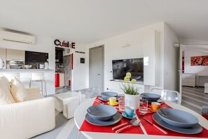 A modern living room with a dining area, a kitchen, and a TV mounted on the wall.