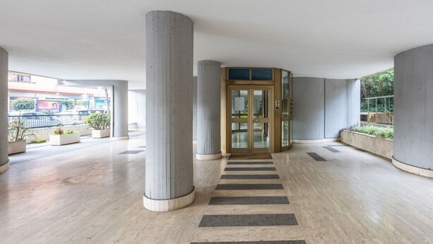 En rymlig entréhall med en central pelare, en glasdörr och utsikt över gatan utanför.