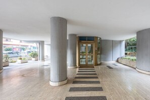 A spacious lobby with a central column, a glass door entrance, and a view of the street outside. - L'Attichetto di Bubi by Rentbeat (Roma)