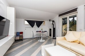 A modern living room with a sofa, a TV, a dining table with chairs, and a kitchen area with cabinets and a window.