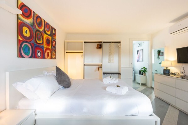 A modern hotel room with a large bed, a wardrobe, a desk, and a TV.