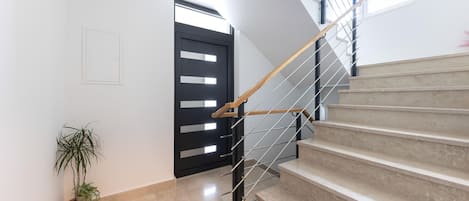 Un escalier moderne avec une main courante en bois et des balustres en métal, menant à un palier agrémenté d’une plante en pot.