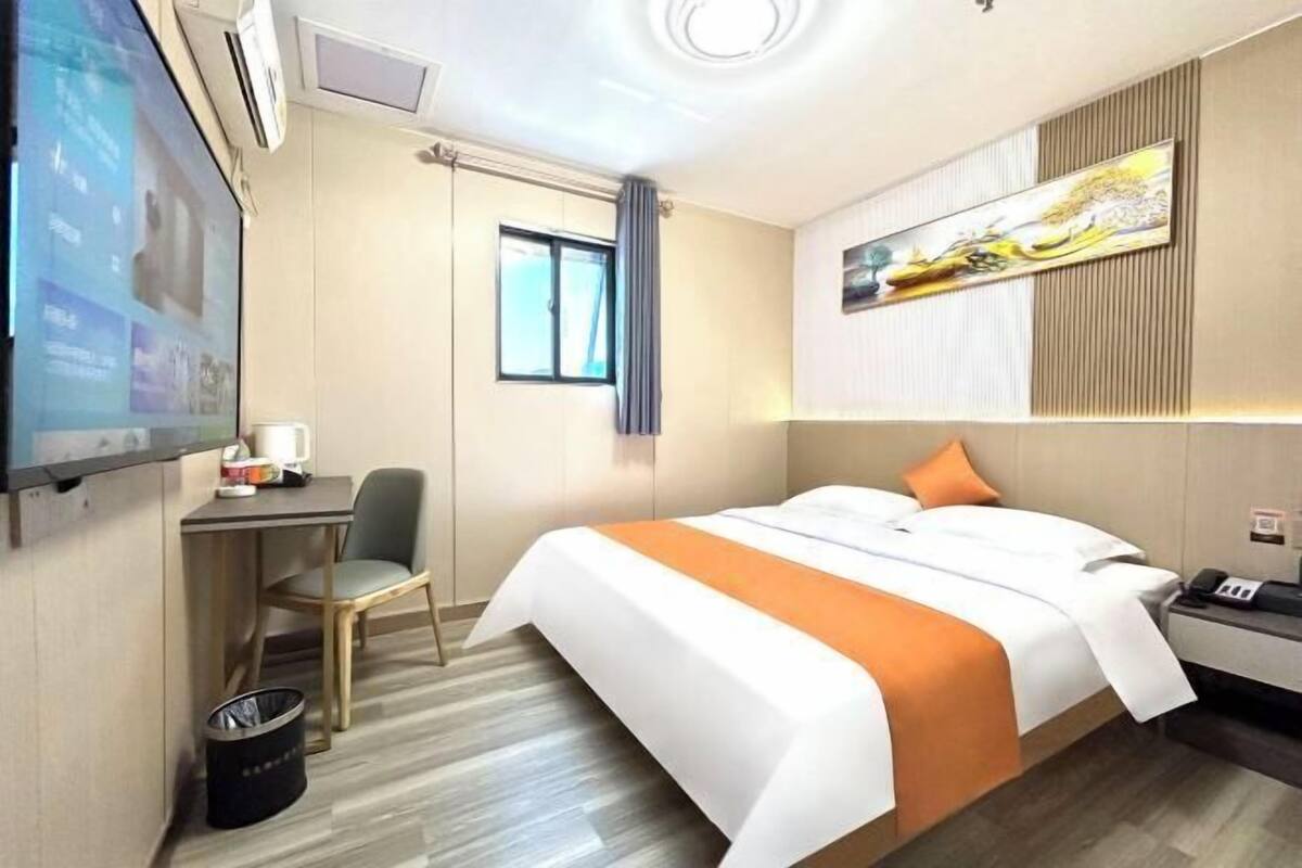 A hotel room with a bed, a desk, a chair, a TV, and a painting on the wall.