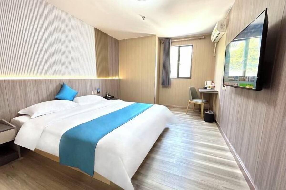 A hotel room with a bed, a desk, a chair, and a TV.
