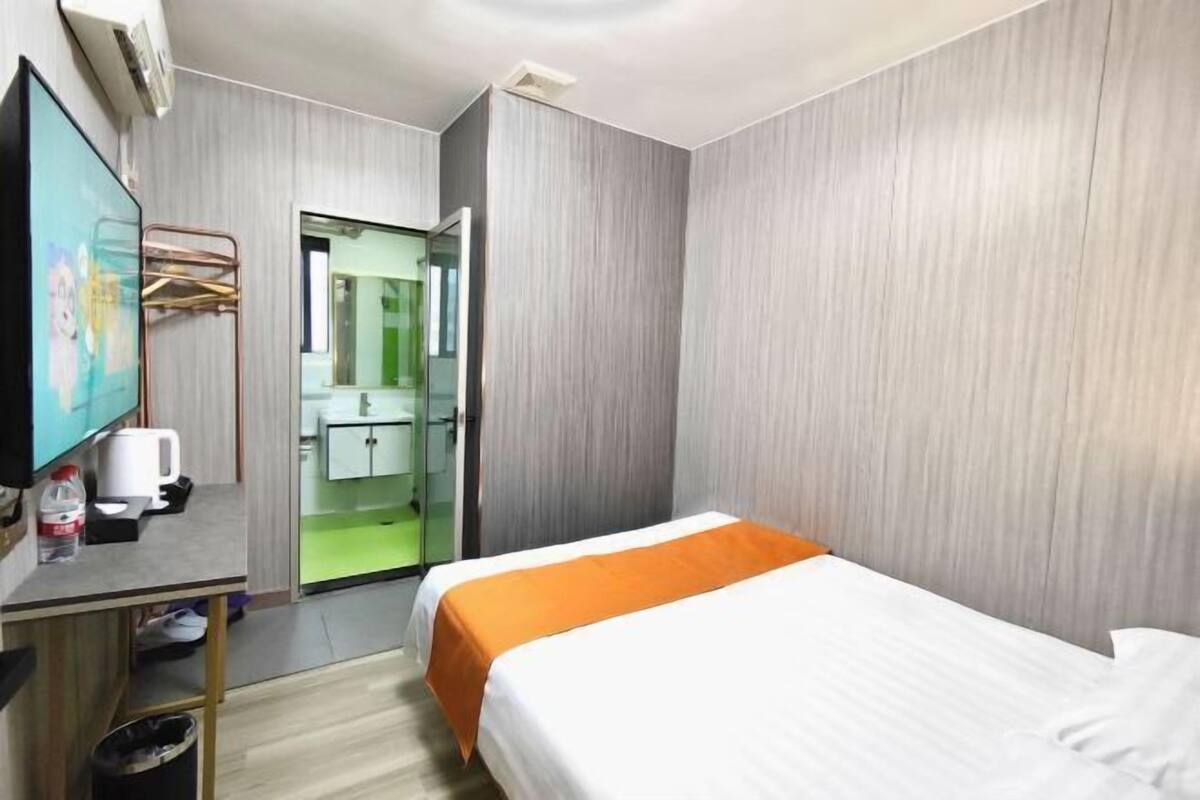 A hotel room with a bed, a desk with a computer, a TV, and a bathroom visible through an open door.