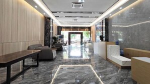 A modern lobby with a marble floor, wooden reception desk, seating area, and a large window. - Meidi Hotel (Shenzhen Bao'an Airport Pingluanshan Metro Station Branch) (Shenzhen)