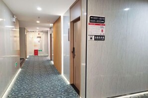 A hotel corridor with a patterned carpet, a wooden door, and a sign with emergency contact information. - Meidi Hotel (Shenzhen Bao'an Airport Pingluanshan Metro Station Branch) (Shenzhen)