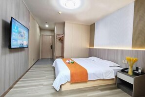 Ein Hotelzimmer mit Bett, Wandfernseher, Nachttisch und einer Tür zu einem Flur.