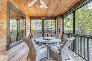 Een overdekt terras met rieten stoelen, een ronde tafel en uitzicht op de omgeving.