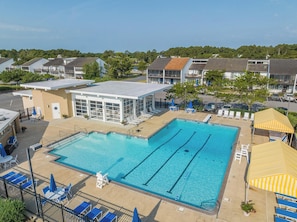 Piscina com espreguiçadeiras e guarda-sóis, rodeada por edifícios.