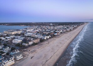 An aerial view of a coastal town with a long beachfront, dense residential buildings, and a clear sky. - Sunspot 100 (Dewey Beach)