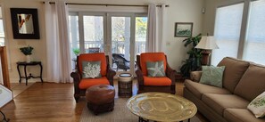 A living room with two armchairs, a brown leather ottoman, a glass coffee table, a sofa, and a view through a glass door. - Dicinson Avenue 7B (Dewey Beach)