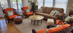 A living room with a brown sofa, orange chairs, a wicker coffee table, and a view of the outdoors. - Dicinson Avenue 7B (Dewey Beach)