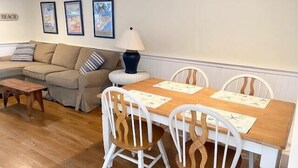 A living room with a sofa, a coffee table, a dining table with chairs, and wall art.
