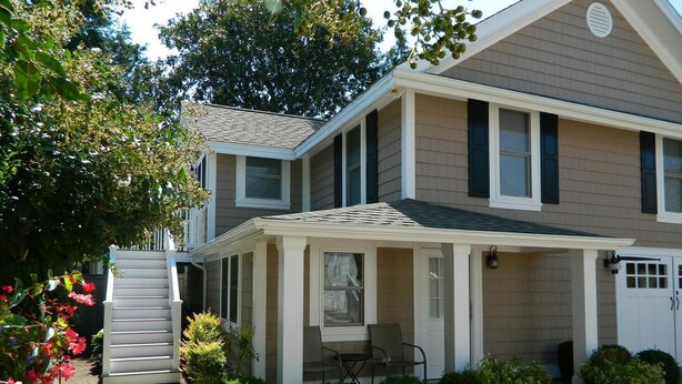 A two-story house with a covered porch, a front door, and a small patio area.