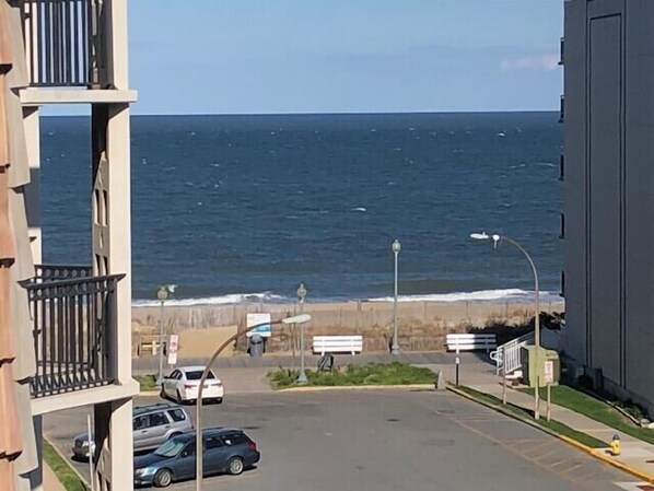 A view of a parking lot with cars, a street lamp, and a building with a balcony overlooking the ocean. - THE Crest 401 (Rehoboth Beach)