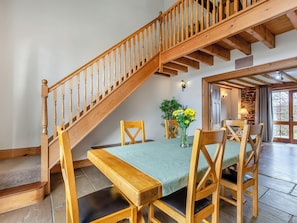 Un coin repas avec un escalier en bois, une table recouverte d’une nappe verte, des chaises en bois et un vase rempli de fleurs.