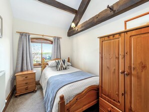 Een slaapkamer met een houten bed, een houten kledingkast, een nachtkastje en een raam met gordijnen.