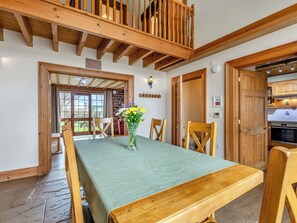 A dining area with a wooden table, chairs, and a vase of flowers. There is a staircase with wooden railings and a view of the outdoors through a glass door. - Barley Store - UK48910 (Allonby)