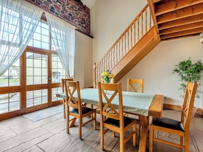 Un coin repas avec une table et des chaises en bois, un escalier et une vue à travers une porte vitrée.