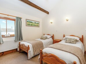 Une chambre avec deux lits en bois, une fenêtre avec des rideaux, un radiateur et un tableau accroché au mur.