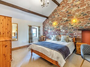 A bedroom with a stone wall, a wooden bed, a chair, and a mirror. - Barley Store - UK48910 (Allonby)